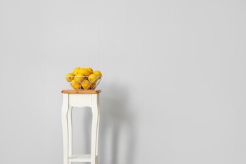 Stand and bowl with lemons near light wall in room