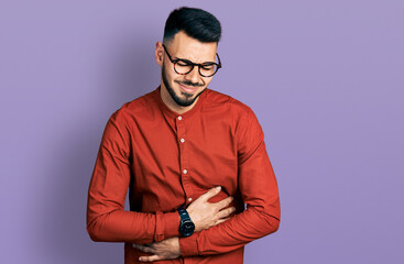 Young hispanic man with beard wearing business shirt and glasses with hand on stomach because indigestion, painful illness feeling unwell. ache concept.