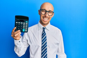 Bald business man with beard showing calculator device looking positive and happy standing and...