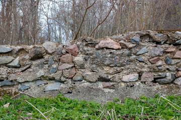 Old cracked concrete house foundation with big and small rocks, bricks and moss