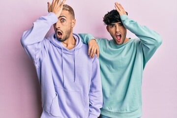 Homosexual gay couple standing together wearing casual clothes surprised with hand on head for...