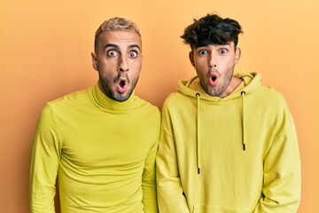 Homosexual gay couple standing together wearing yellow clothes afraid and shocked with surprise expression, fear and excited face.