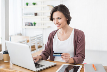 Obraz na płótnie Canvas Young woman holding credit card and using laptop computer at home, Businesswoman or entrepreneur working, Online shopping, e-commerce, internet banking, spending money concept