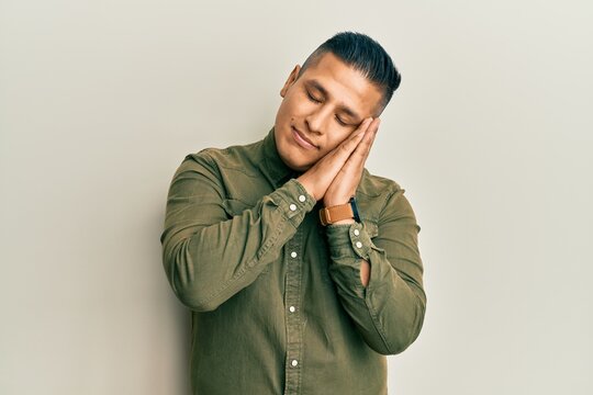 Young latin man wearing casual clothes sleeping tired dreaming and posing with hands together while smiling with closed eyes.