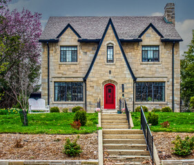 Vintage rock block house with dormers and large front paned  windows on hill with step leading up drom street in  spring