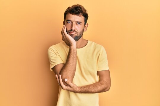 Handsome man with beard wearing casual yellow tshirt over yellow background thinking looking tired and bored with depression problems with crossed arms.
