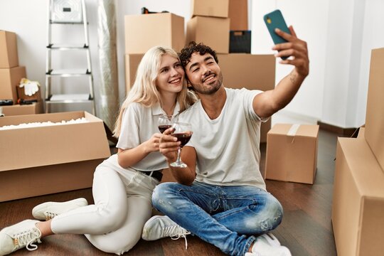 Young beautiful couple toasting with red wine and making selfie at new home