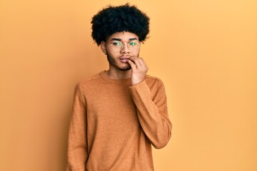 Fototapeta na wymiar Young african american man with afro hair wearing casual winter sweater looking stressed and nervous with hands on mouth biting nails. anxiety problem.