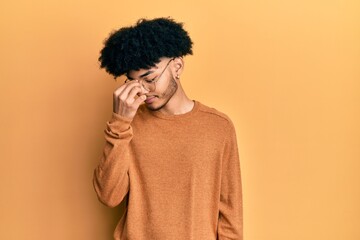 Obraz na płótnie Canvas Young african american man with afro hair wearing casual winter sweater tired rubbing nose and eyes feeling fatigue and headache. stress and frustration concept.