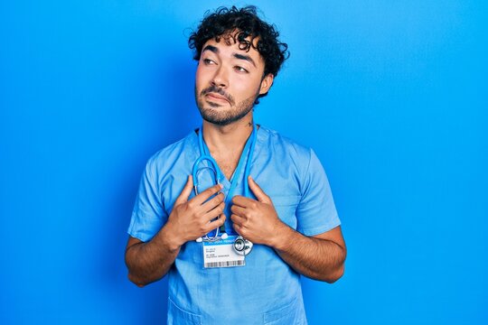 Young hispanic man wearing blue male nurse uniform smiling looking to the side and staring away thinking.