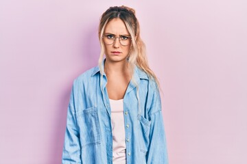 Beautiful young blonde woman wearing casual clothes and glasses skeptic and nervous, frowning upset because of problem. negative person.