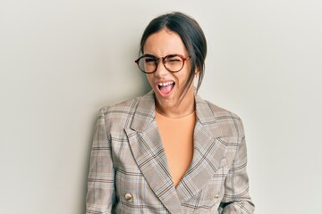 Young brunette woman wearing business jacket and glasses winking looking at the camera with sexy expression, cheerful and happy face.