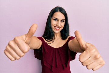 Young hispanic woman wearing casual clothes approving doing positive gesture with hand, thumbs up smiling and happy for success. winner gesture.
