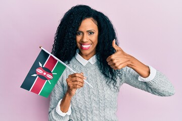 Middle age african american woman holding kenya flag smiling happy and positive, thumb up doing excellent and approval sign