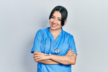 Beautiful hispanic woman wearing doctor uniform and stethoscope happy face smiling with crossed arms looking at the camera. positive person.