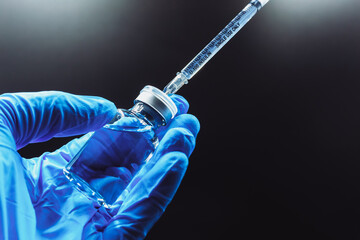 The vaccine concept is in the hands of a doctor's white vaccine bottle and a blue glove with copy space, isolated on black background