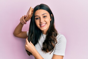 Young hispanic woman styling hair using comb smiling with a happy and cool smile on face. showing teeth. - obrazy, fototapety, plakaty