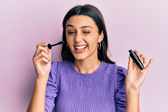 Young hispanic woman holding eyelashes curler winking looking at the camera with sexy expression, cheerful and happy face.