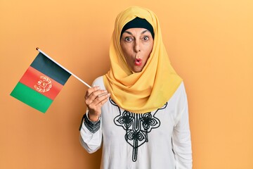 Middle age hispanic woman holding afghanistan flag scared and amazed with open mouth for surprise, disbelief face