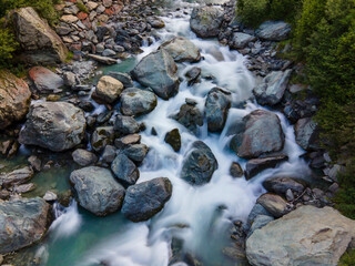 Aerial long exposure of alpine river in the mountain, silk effect, flowing water	