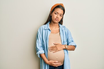 Beautiful hispanic woman expecting a baby, touching pregnant belly looking sleepy and tired,...