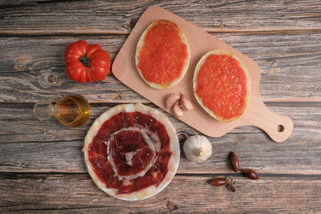 Breakfast of bread toasts with acorn-fed Iberian ham, tomato, garlic and olive oil (tumaca bread) on dark gray background