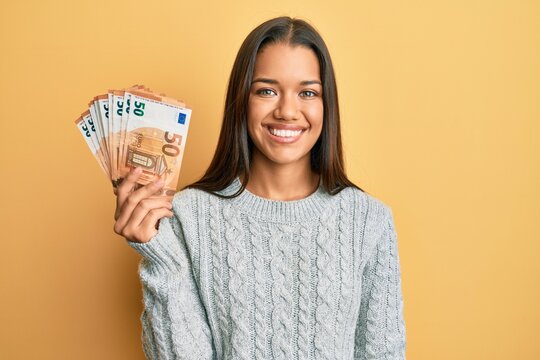 Beautiful hispanic woman holding bunch of 50 euro banknotes looking positive and happy standing and smiling with a confident smile showing teeth