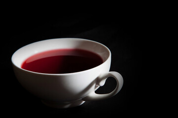 A white teacup with red berry tea. A black background