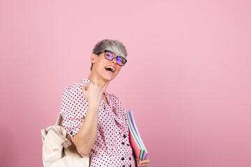 Stylish woman in dress and glasses on pink background with notebooks clenching fist winner gesture gesture education concept