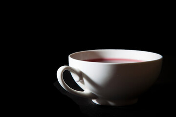 A white teacup with red berry tea. A black background