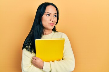 Beautiful hispanic woman with nose piercing holding book smiling looking to the side and staring away thinking.