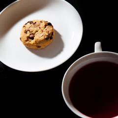 White cup of berry tea and cookie on the white plate. Black background