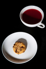White cup of berry tea and cookie on the white plate. Black background