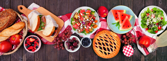 Summer picnic food table scene overhead view on a wood banner background. Variety of cold salads,...