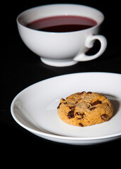 White cup of berry tea and cookie on the white plate. Black background
