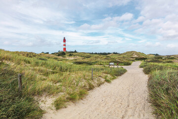 Tall red and white striped lighthouse building standing on small hill. Sandy coastal landscape with...