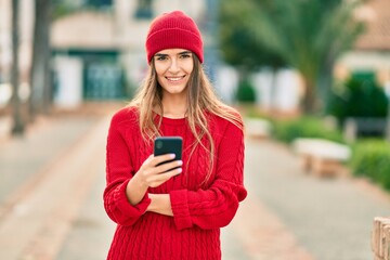 Young hispanic woman wearing winter style using smartphone at the city.
