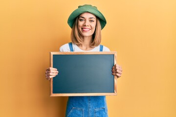 Young caucasian blonde woman holding blackboard smiling with a happy and cool smile on face. showing teeth.