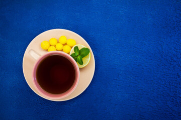 cup of tea with lemon, round candies and a mint leaf, a blue textured background and a copy space