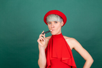 Studio portrait of stylish woman in red dress on green background with electronic cigarette IQOS...
