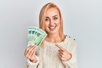 Beautiful caucasian woman holding 10000 south korean won banknotes smiling happy pointing with hand and finger