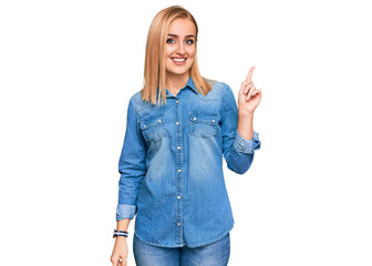 Beautiful caucasian woman wearing casual denim jacket with a big smile on face, pointing with hand and finger to the side looking at the camera.