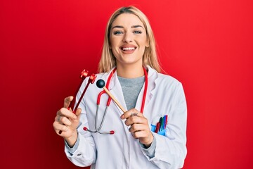 Young caucasian woman wearing doctor uniform holding tuning fork smiling with a happy and cool...