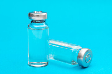 Two glass vials of vaccine on blue background. Close up.