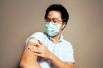 Asian man got covid-19 vaccine. Young asian male looking at his arm happily after getting his first vaccine shot. Teenage received his first vaccine dose,Man cured his illness and disease condition