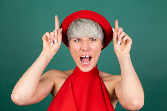 Studio portrait of stylish woman in red dress on green background funny crazy does cow gesture