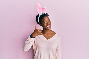 Young african american girl wearing cute easter bunny ears smiling doing phone gesture with hand and fingers like talking on the telephone. communicating concepts.