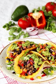 Mexican tacos with roast minced meat with corn and black beans, onions, fresh tomatoes, paprika and cilantro are flavored with guacamole sauce.