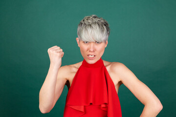 Studio portrait of stylish woman in red dress on green background angrily, reproachfully accuses...