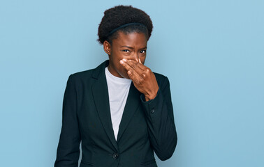 Young african american girl wearing business clothes smelling something stinky and disgusting, intolerable smell, holding breath with fingers on nose. bad smell